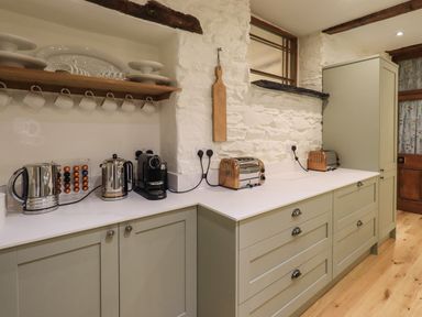 A kitchen countertop with kettles coffee machine toasters and wooden shelves with cups and plates at Stepping Stones House in Ambleside