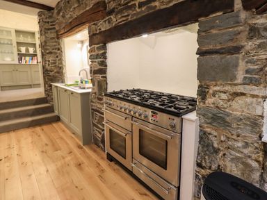 A kitchen with a stainless steel stove set into a stone wall and a sink with cabinets next to it at Stepping Stones House in Ambleside