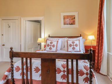 A bedroom with a wooden bed framed by red and white quilt and pillows with a floral painting on the wall at Stepping Stones House in Ambleside