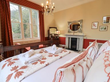A bedroom with a bed with folded towels a fireplace a mirror a dresser and a window with curtains at Stepping Stones House Ambleside