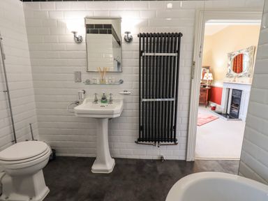 A bathroom with a toilet pedestal sink radiator and view into a room with a fireplace at Stepping Stones House Ambleside