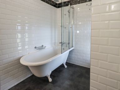 A bathroom with a clawfoot bathtub and glass shower screen with white tiled walls at Stepping Stones House in Ambleside