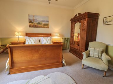 A bedroom with a wooden bed, bedside tables with lamps, a wardrobe, and an armchair at Stepping Stones House in Ambleside
