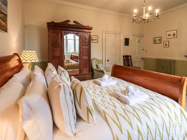 A bedroom with a wooden bed and wardrobe an armchair and framed pictures on the wall at Stepping Stones House in Ambleside