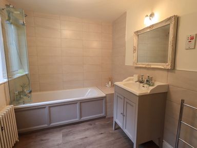 A bathroom with a bathtub shower unit and a sink with a mirror at Stepping Stones House in Ambleside