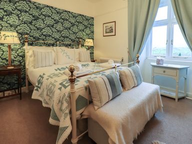 A bedroom with a bed, pillows, lamps, window with curtains, and a small table at Stepping Stones House in Ambleside