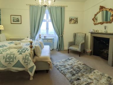 A bedroom with a bed bench armchair rug fireplace and window with curtains at Stepping Stones House Ambleside