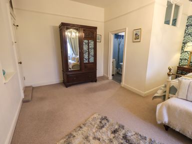 A bedroom with a wooden wardrobe a partial view of a bed and an open door to a bathroom at Stepping Stones House in Ambleside