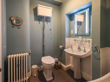 A bathroom with a toilet a pedestal sink a mirror a radiator and a wicker basket at Stepping Stones House in Ambleside