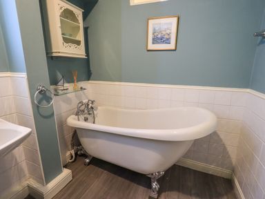 A bathroom with a clawfoot bathtub a wall cabinet and a framed picture at Stepping Stones House in Ambleside