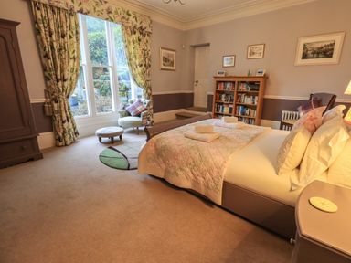 A bedroom with a bed towels on it a bookshelf chair and floral curtains at Stepping Stones House in Ambleside
