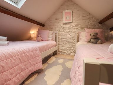A bedroom with two single beds with pink bedding teddy bears on the beds a skylight and a stone wall at Stepping Stones House Ambleside
