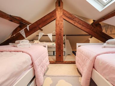 A bedroom with two single beds with pink bedding and wooden beams on the ceiling at Stepping Stones House in Ambleside
