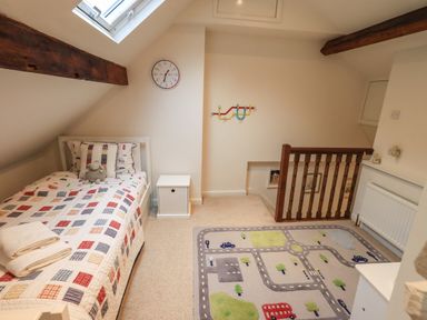 A small bedroom with a single bed a bedside table a wall clock a colorful rug featuring roads and vehicles and wooden beams at Stepping Stones House in Ambleside