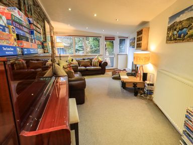 A living room with a piano sofa pillows lamp coffee table and large windows at Stepping Stones House Ambleside