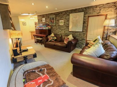 A living room with leather sofas a piano and a lamp on a stone wall at Stepping Stones House in Ambleside