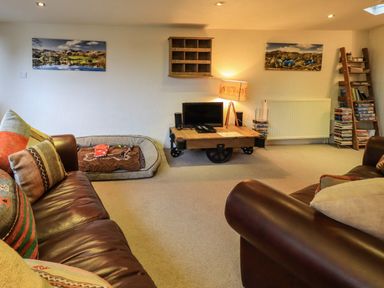 A living room with two leather sofas a coffee table with a lamp and a TV a dog bed two landscape pictures on the wall and a bookshelf with DVDs at Stepping Stones House Ambleside