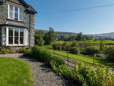 A stone house with a gravel path and garden overlooking fields and hills at Stepping Stones House in Ambleside