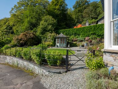 A private garden with a gravel path green lawn and a small gazebo behind a metal gate at Stepping Stones House in Ambleside
