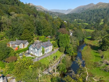 A countryside stone house near a river surrounded by trees and hills at Stepping Stones House in Ambleside