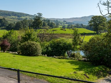 A grassy backyard with bushes a small pond and hills in the background at Stepping Stones House in Ambleside