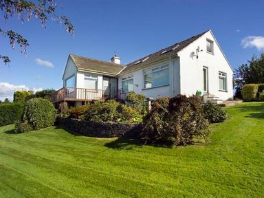 White house with sloped roof surrounded by green grass and bushes under a blue sky at Primrose Mount in Bowness