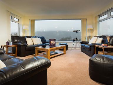 A living room with black leather sofas wooden tables a coffee table and a telescope at Primrose Mount in Bowness