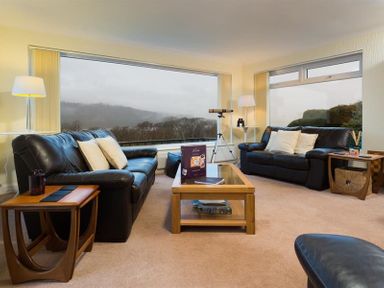 A living room with leather sofas coffee table telescope and large windows at Primrose Mount in Bowness