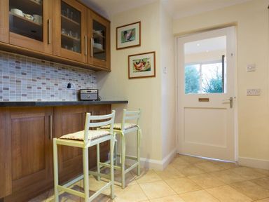 A kitchen with wooden cabinets two chairs a tiled floor and a white door at Primrose Mount in Bowness