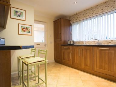 A kitchen with wooden cabinets two green bar stools and framed pictures on the wall at Primrose Mount in Bowness