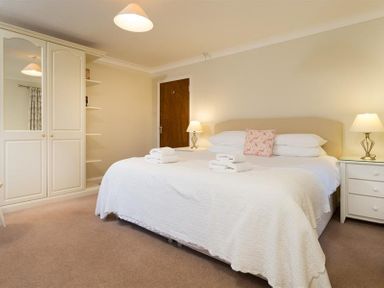 A bedroom with a large bed white bedding two bedside tables with lamps and a wardrobe at Primrose Mount in Bowness