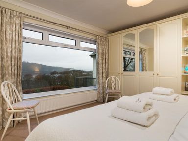 A bedroom with a large window two chairs wardrobes and towels on the bed at Primrose Mount in Bowness