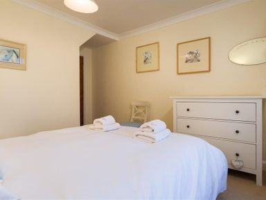 A bedroom with a bed with folded towels a white chest of drawers a chair and framed pictures at Primrose Mount in Bowness