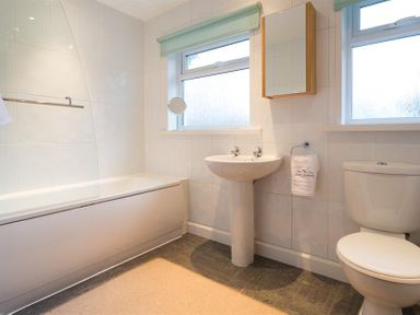 A bathroom with a bathtub a sink a toilet two windows and a wall cabinet at Primrose Mount in Bowness