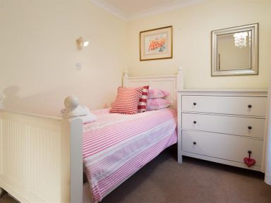 A bedroom with a single bed with striped bedding next to a white chest of drawers with a mirror above at Primrose Mount in Bowness