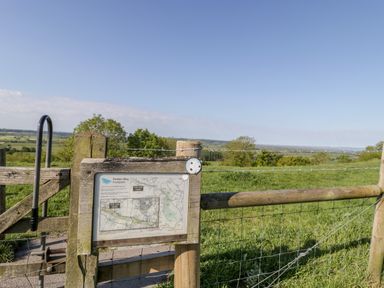 A wooden gate with a map sign and metal stile overlooking fields and trees at Old Cary Cottage in Henley near Langport