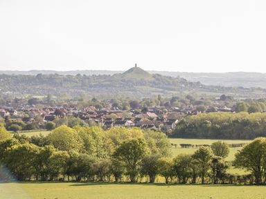 A countryside view with trees fields and a town with a hill and tower in the background at Old Cary Cottage Henley near Langport