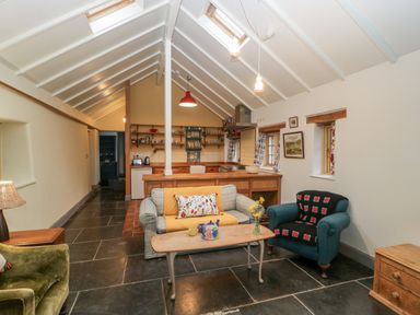 A living area with a sofa, armchairs, coffee table, and a kitchen in the background at Old Cary Cottage Henley near Langport