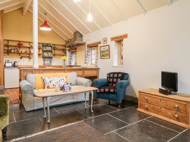 A living room with a sofa and armchair a coffee table and a television on a wooden cabinet at Old Cary Cottage Henley near Langport