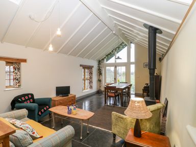 A room with a seating area including chairs and sofa a dining table near large windows and a wood stove at Old Cary Cottage Henley near Langport