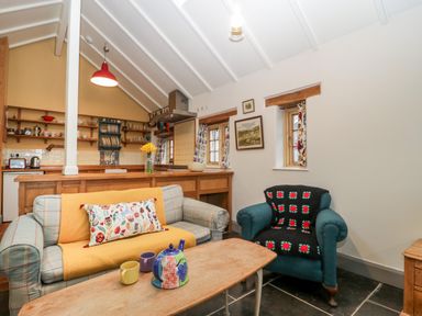 A living room with a sofa and armchair and a wooden coffee table in front of a kitchen area at Old Cary Cottage in Henley near Langport