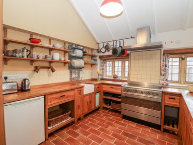 A kitchen with wooden cabinets shelves dish rack stove and windows at Old Cary Cottage Henley near Langport