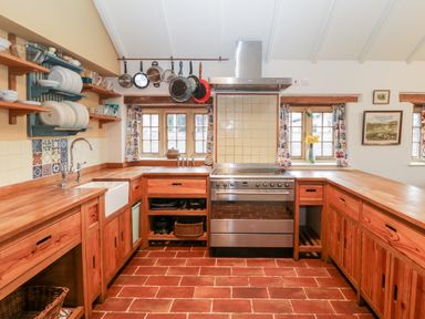 A kitchen with wooden countertops and cabinets a stainless steel stove hanging pots and pans and tiled flooring at Old Cary Cottage Henley near Langport