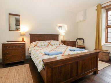 A bedroom with a wooden bed and nightstands two lamps a chair and a window at Old Cary Cottage Henley near Langport