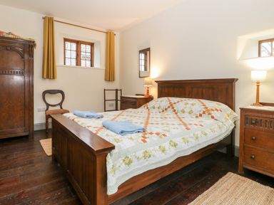 A bedroom with a wooden bed with a patchwork quilt two blue towels bedside tables lamps an armoire a chair and two small windows at Old Cary Cottage Henley near Langport