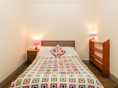 A bedroom with a double bed wooden headboard side table red lamp wooden bookshelf with lamp at Old Cary Cottage Henley near Langport