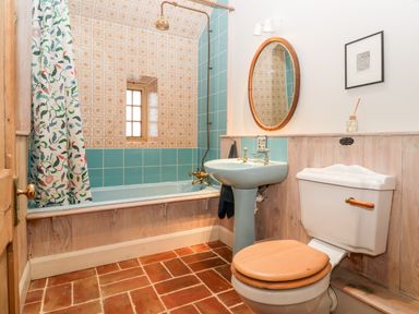 A bathroom with a bathtub shower combination blue sink toilet with wooden seat and a circular mirror at Old Cary Cottage Henley near Langport