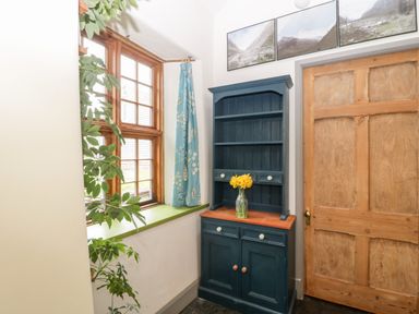 A corner with a wooden door a blue cabinet with a vase of yellow flowers wooden framed windows with a blue curtain and a green windowsill at Old Cary Cottage Henley near Langport
