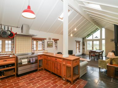 A kitchen and dining area with wooden cabinets a stove and tiled floor at Old Cary Cottage Henley near Langport