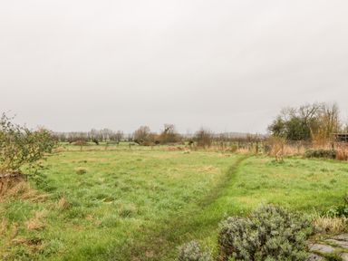 A grassy field with a narrow path and sparse bushes under an overcast sky at Old Cary Cottage Henley near Langport